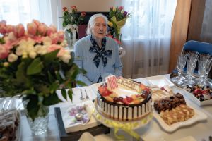 jubilatka Genowefa Kozieł w swoim pokoju, kwiaty i tort urodzinowy na stole