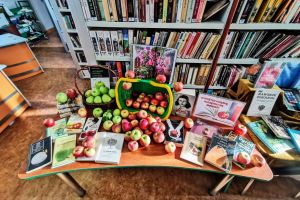 stolik z książkami i jabłkami, za nimi regał z książkami