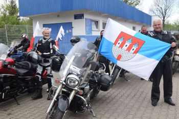 kilkunastu rawskich motocyklistów stoją z motorami i flagą...