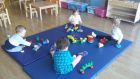 dzieci w żłobku siedzą w dystansie na materacach, wokół zabawki