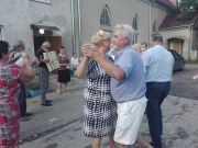 grupa emerytów tańczy przed budynkiem, w tle akordeonista