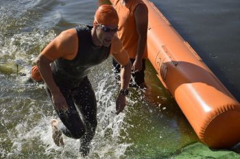 triathlonista w pomarańczowym czepku wybiega z wody