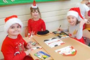 troje dzieci koloruje św. Mikołaja na kartonie