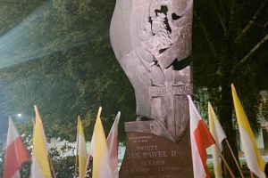 pomnik św. Jana Pawła II, pod pomnikiem flagi biało-żółte...